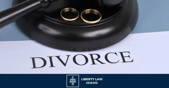 A gavel and two wedding rings are placed on a document titled "DIVORCE." The image includes the text "LIBERTY LAW IDAHO."
